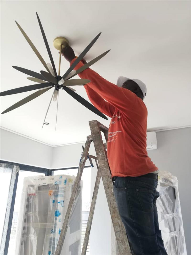 Electrician installing a ceiling fan from a ladder