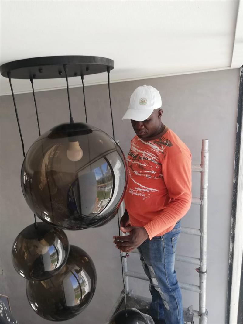 Electrician fitting a large pendant light near a window