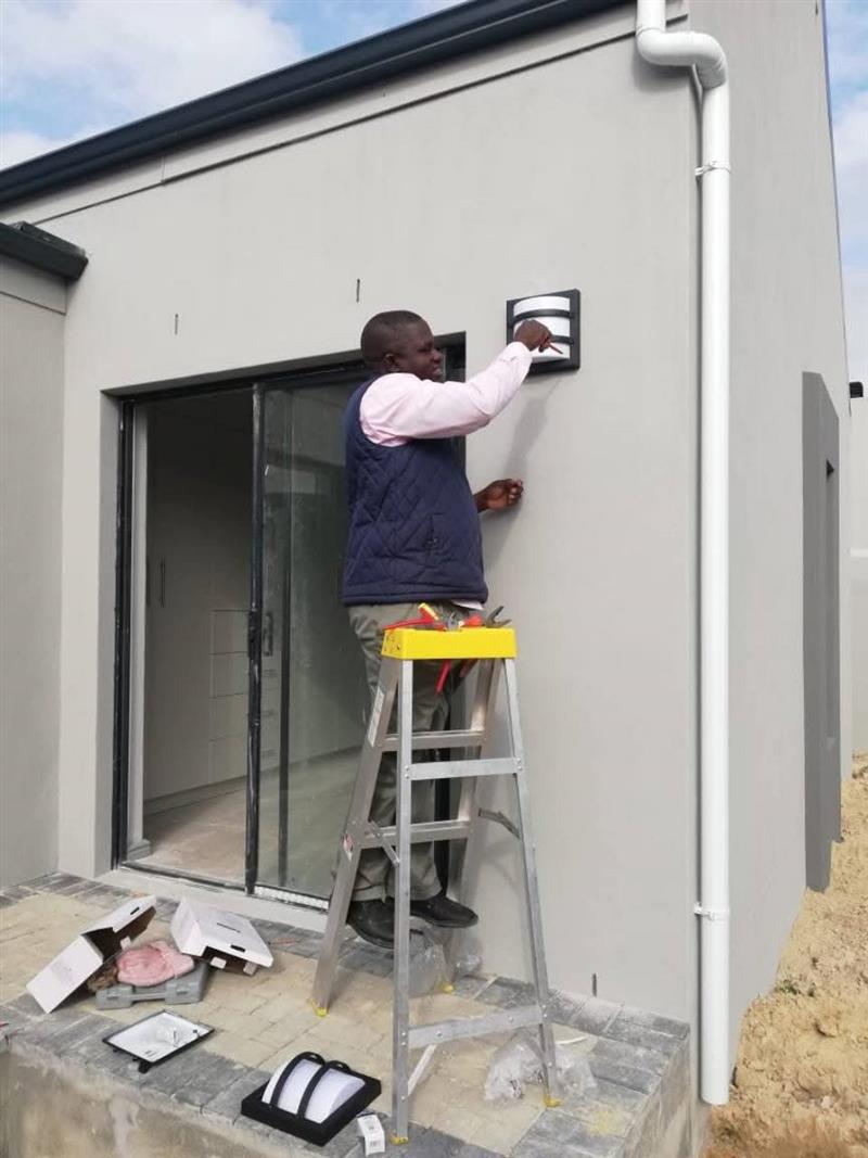 Electrician installing an outdoor wall light on a home exterior